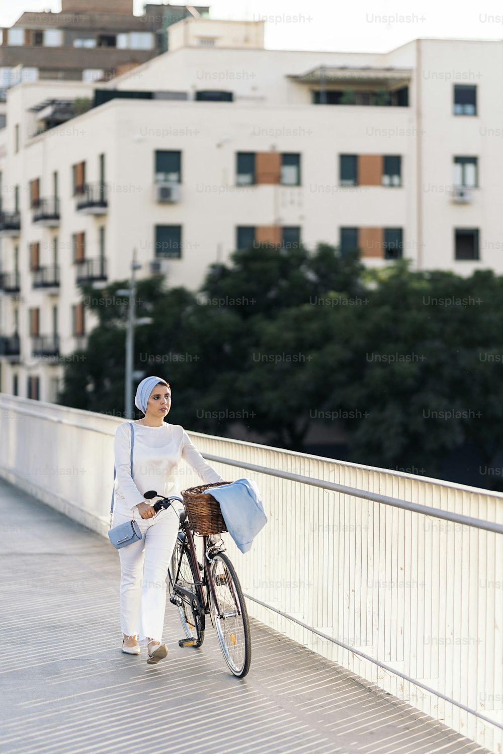 Cheerful muslim woman walking with her bicycle next to her on the footbridge in a sunny day.