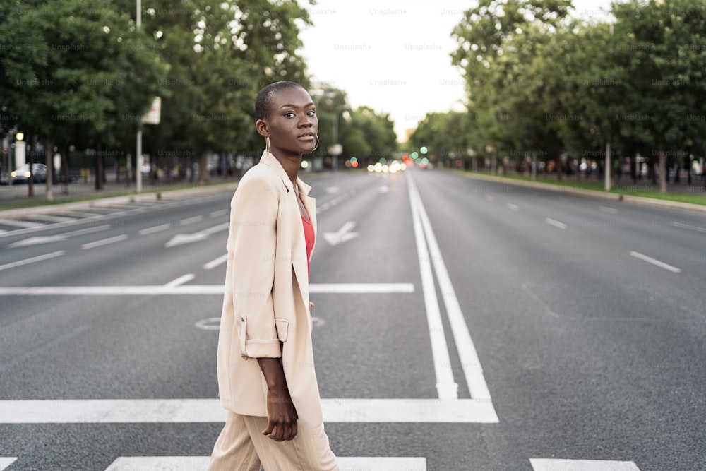 Stylish young adult woman with short hair looking at camera crossing the street in the city