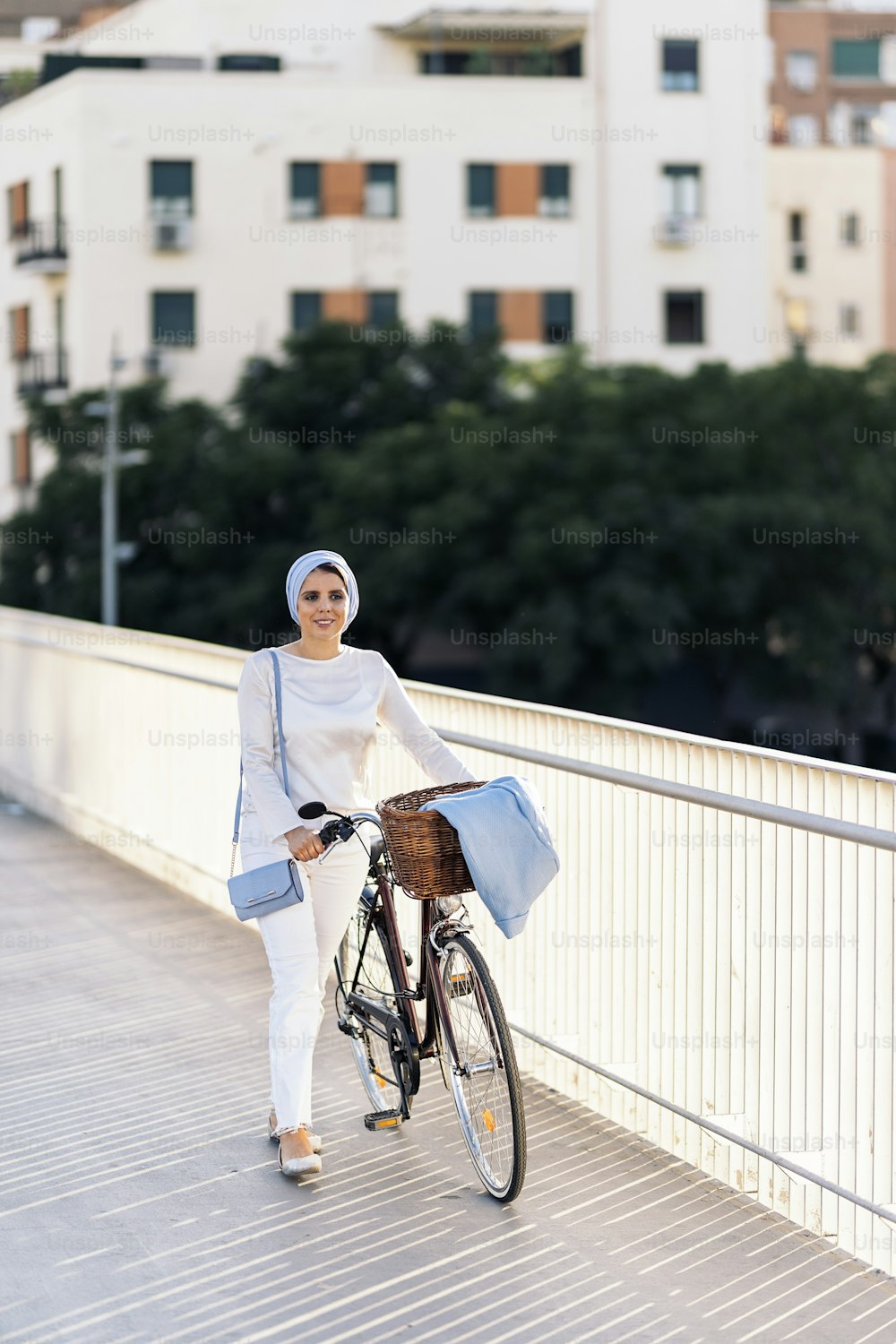 Vertical image of a muslim woman walking with her bicycle on the sidewalk looking away in a sunny day.