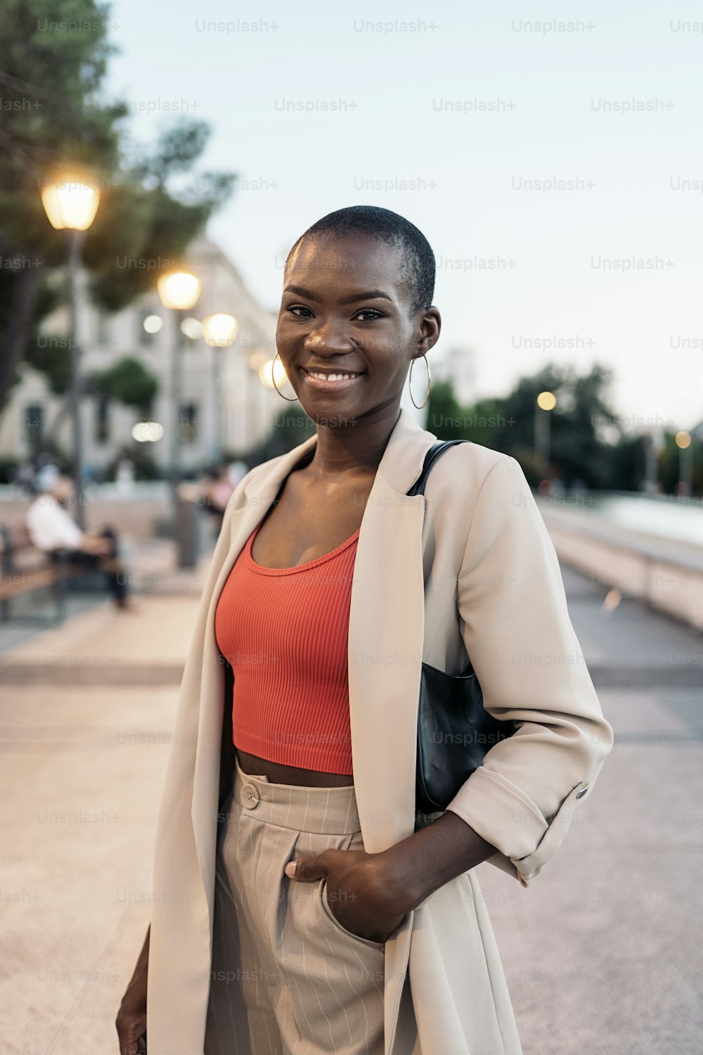 Front view of a fashionable african american young adult woman laughing while standing in the city at sunset