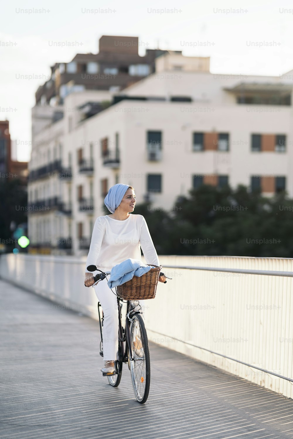 Vertical image of a muslim woman riding her bicycle on the sidewalk looking away in a sunny day.