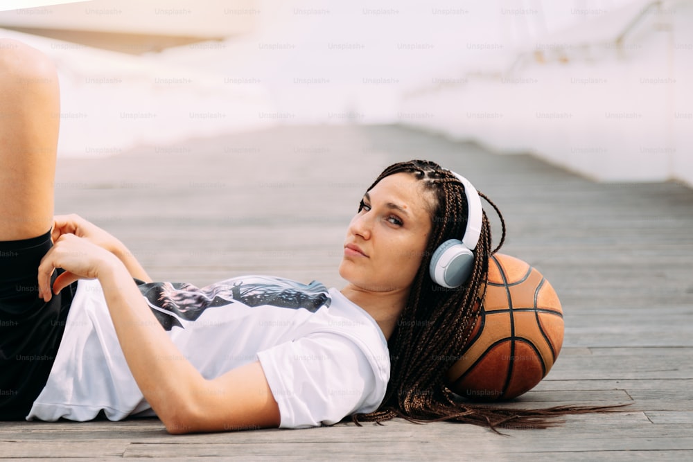 Femme sérieuse allongée avec un ballon de basket et écoutant de la musique en regardant la caméra.