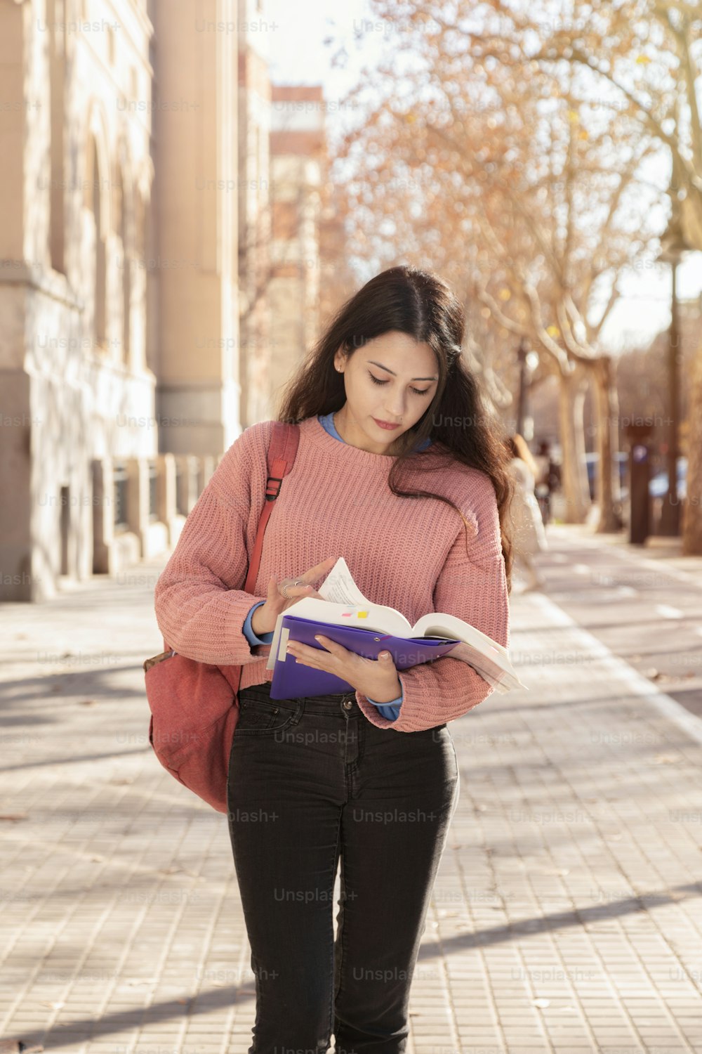Concentrated woman studying for college. Student girl reading a book on the street. Back to class. latin gril. Pink color