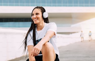 Lächelnde Frau mit Zöpfen im Haar und Kopfhörern, die in ihrer Zeit Musik hört und auf den Horizont blickt. Horizontales Lifestyle-Foto. Gemischtrassiges Mädchen