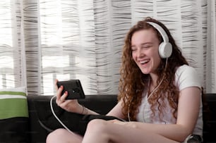 Jeune fille rousse souriante regardant un téléphone portable avec des écouteurs.