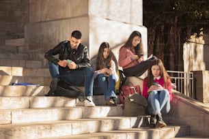 Four students sitting on the stairs using their mobile phones. Concept communication, university, technology