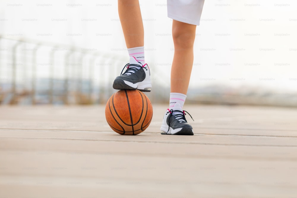 Dettaglio ravvicinato delle scarpe da ginnastica di una donna che calpestano un pallone da basket. Profondità di campo ridotta con spazio di copia