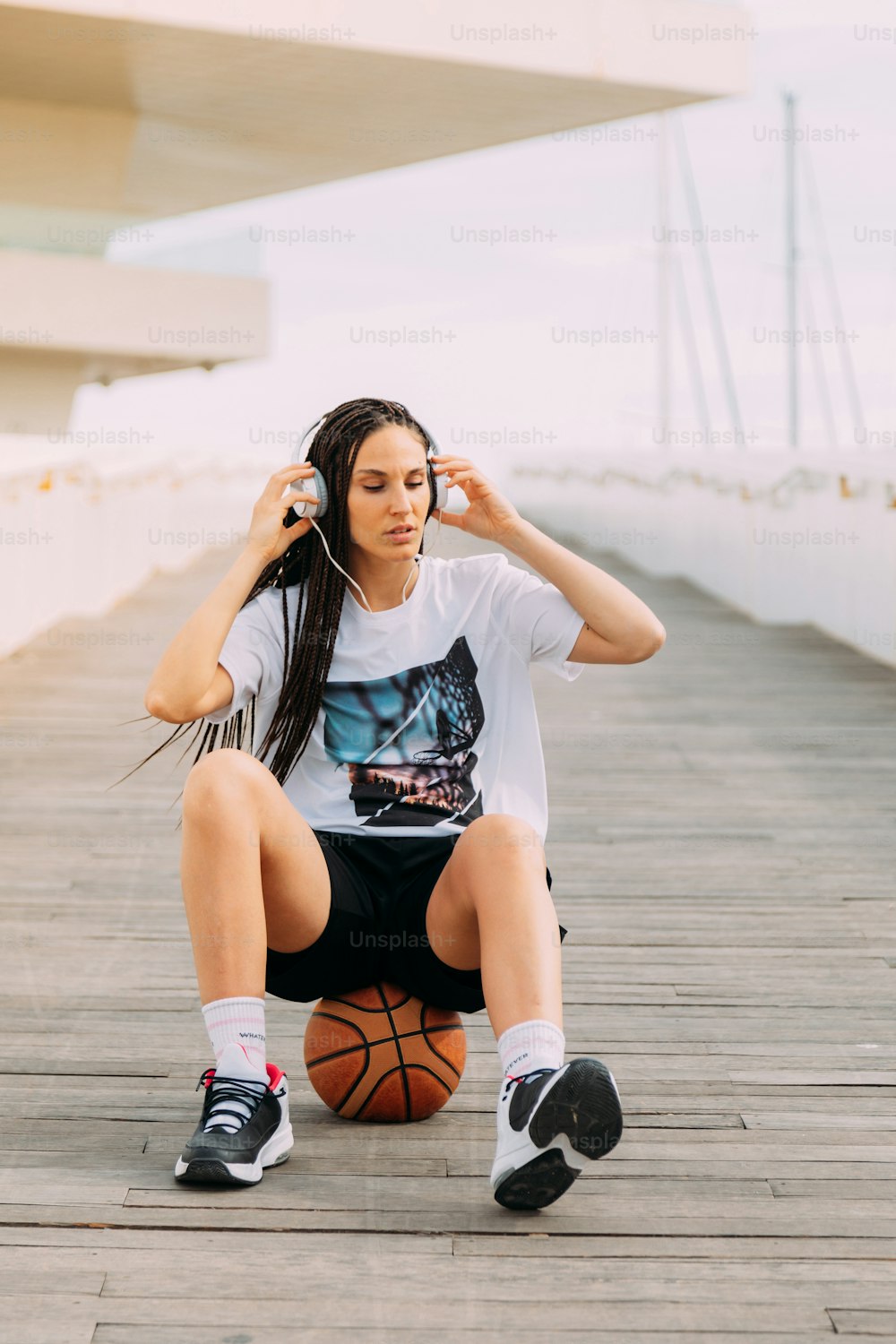 Girl with braids and headphones sitting on top of a basketball. Sport and music. lifestyle and real people.