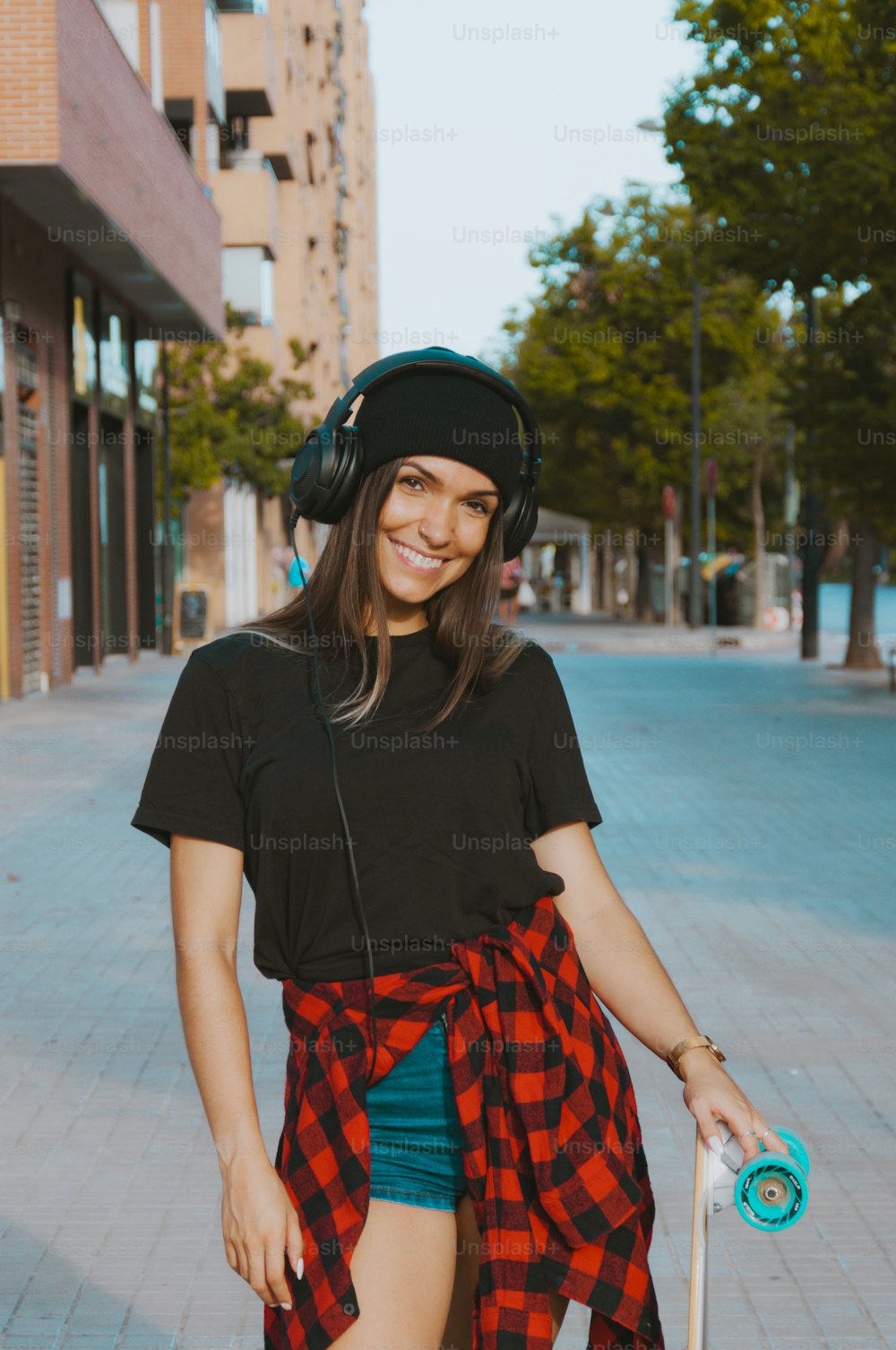 Portrait of a skate woman looking at you smiling. Girl in urban dress with headphones and skateboard.