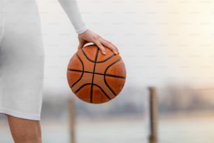 Close-up de uma mão segurando uma bola de basquete com a cidade ao fundo