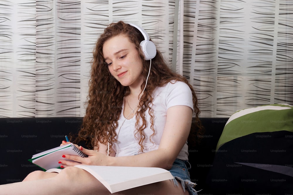 自宅の居間に座ってヘッドフォンで音楽を聴きながら勉強している若い学生女の子。学校に戻る