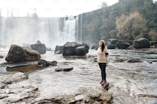Joven latina de pie junto a un río con una cascada al fondo