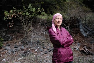 Frau mit rosafarbenem Kopftuch, hat Krebs und ruht sich mitten im Wald aus