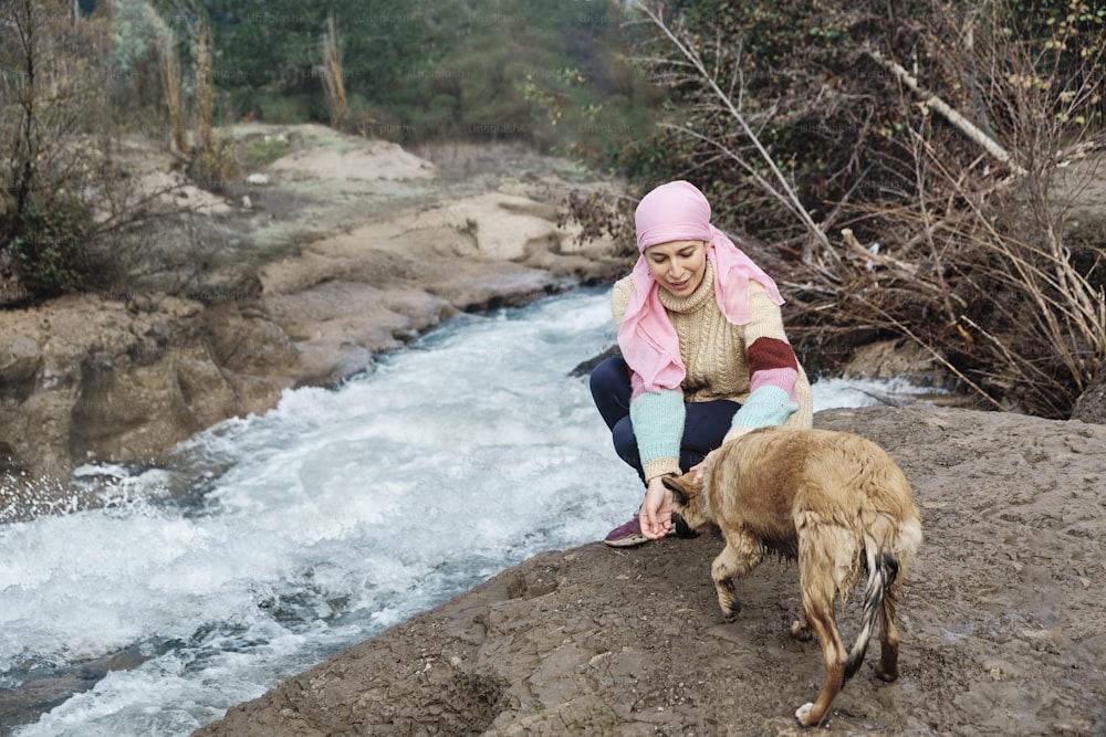 Mujer joven con cáncer jugando con un perro en la orilla de un río