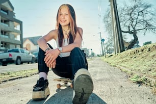 Menina sorridente sentada em um skate na cidade durante o pôr do sol