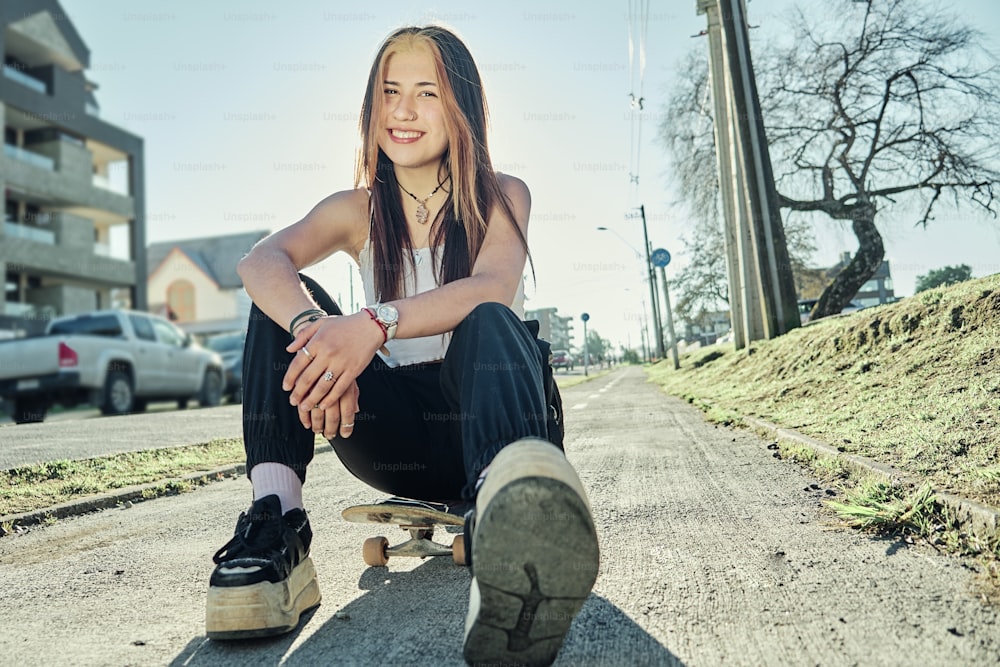 Smiling girl sitting on a skateboard in the city during sunset