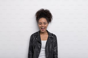 Femme brune riante avec les yeux fermés sur un mur blanc