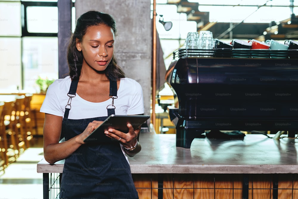 Young barista using digital tablet. Waitress standing by the coffee machine.