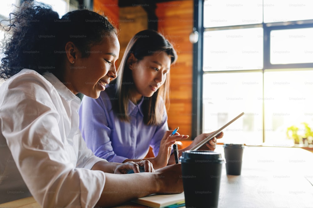 Zwei Geschäftsfrauen, die sich über ein digitales Tablet unterhalten, während sie in einem Café arbeiten
