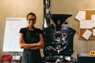 Barista debout à côté de la machine à torréfier le café dans le café. Propriétaire d’entreprise souriant regardant une caméra.