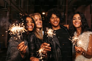 Four young friends celebrating new years eve with sparklers, standing together on street