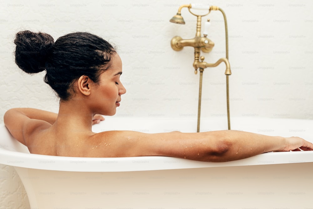 Side view of female relaxing in bathtub with her eyes closed