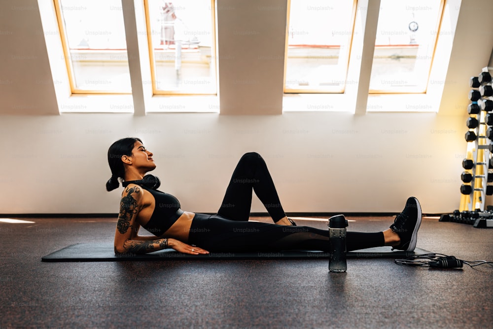 Young woman wearing sports clothes lying on mat in gym relaxing between sets