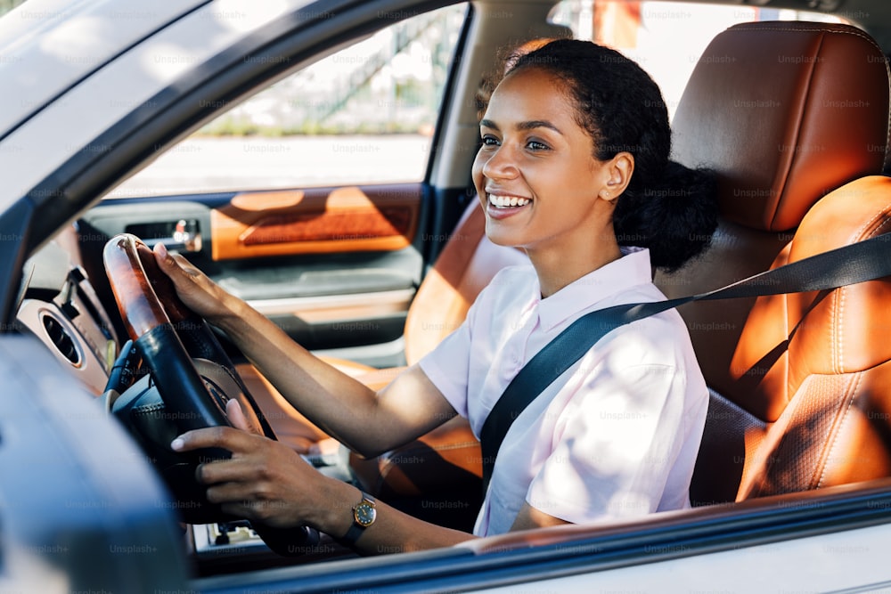 Mujer sonriente conduciendo mirando por la ventana de un coche. Mujer feliz sosteniendo un volante en el vehículo.