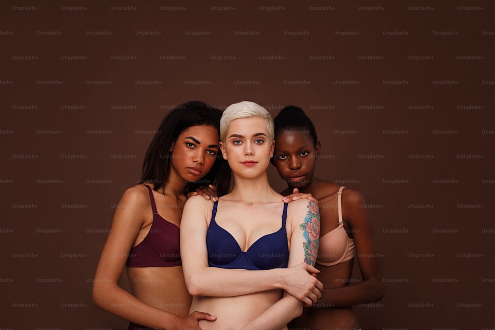 肌色の異なる3人の女性が一緒に立っています。背景にランジェリーを着た若い女性のグループ。