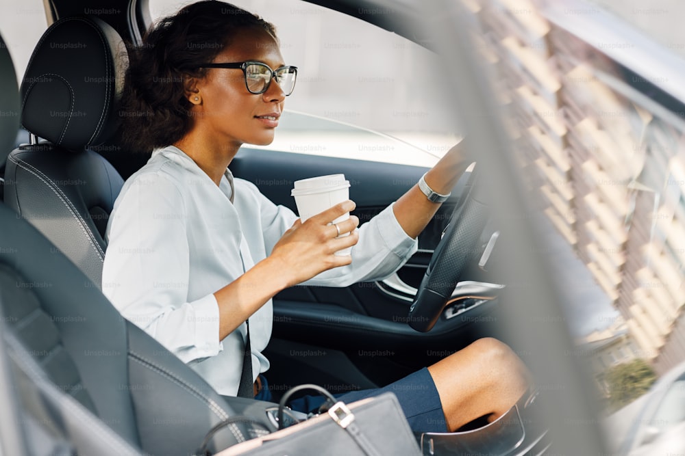 Donna d'affari seduta in auto. Vista laterale dell'autista femminile che tiene un caffè.
