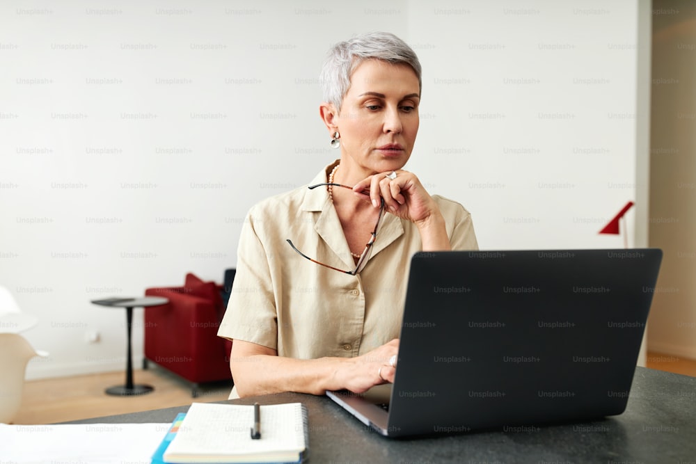 Mature adult female holding glasses typing on a laptop