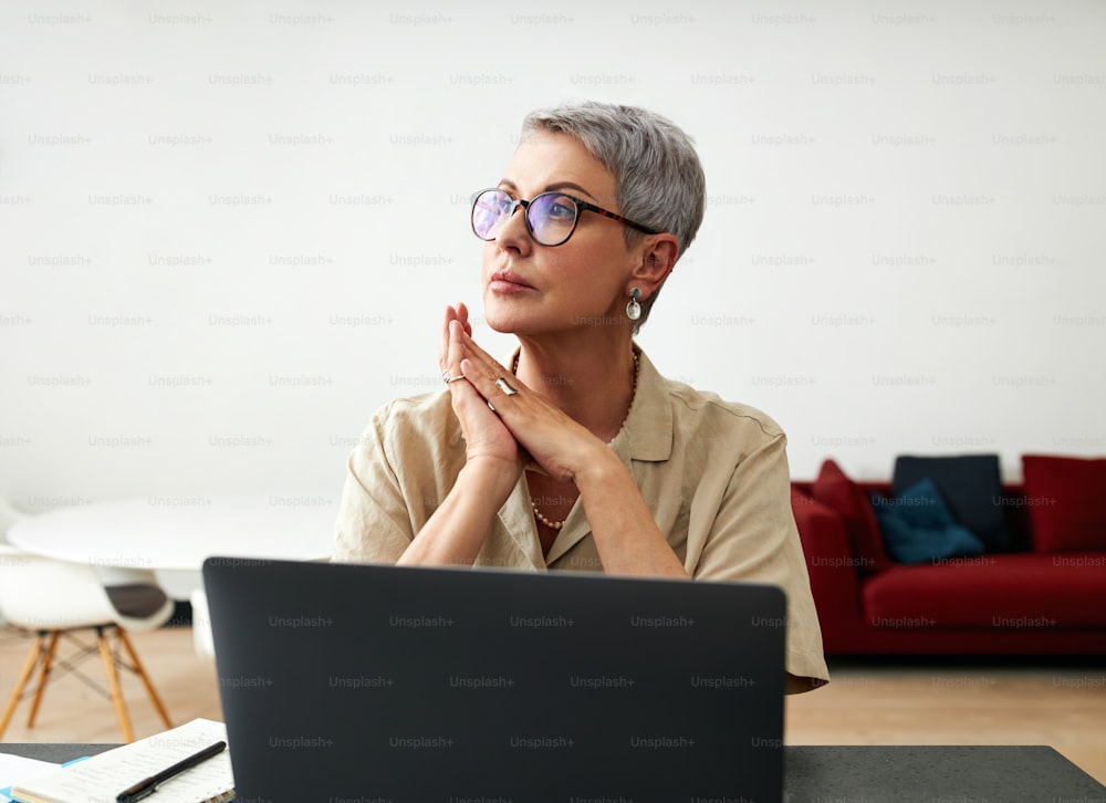 Stylish mature woman in glasses sitting at desk