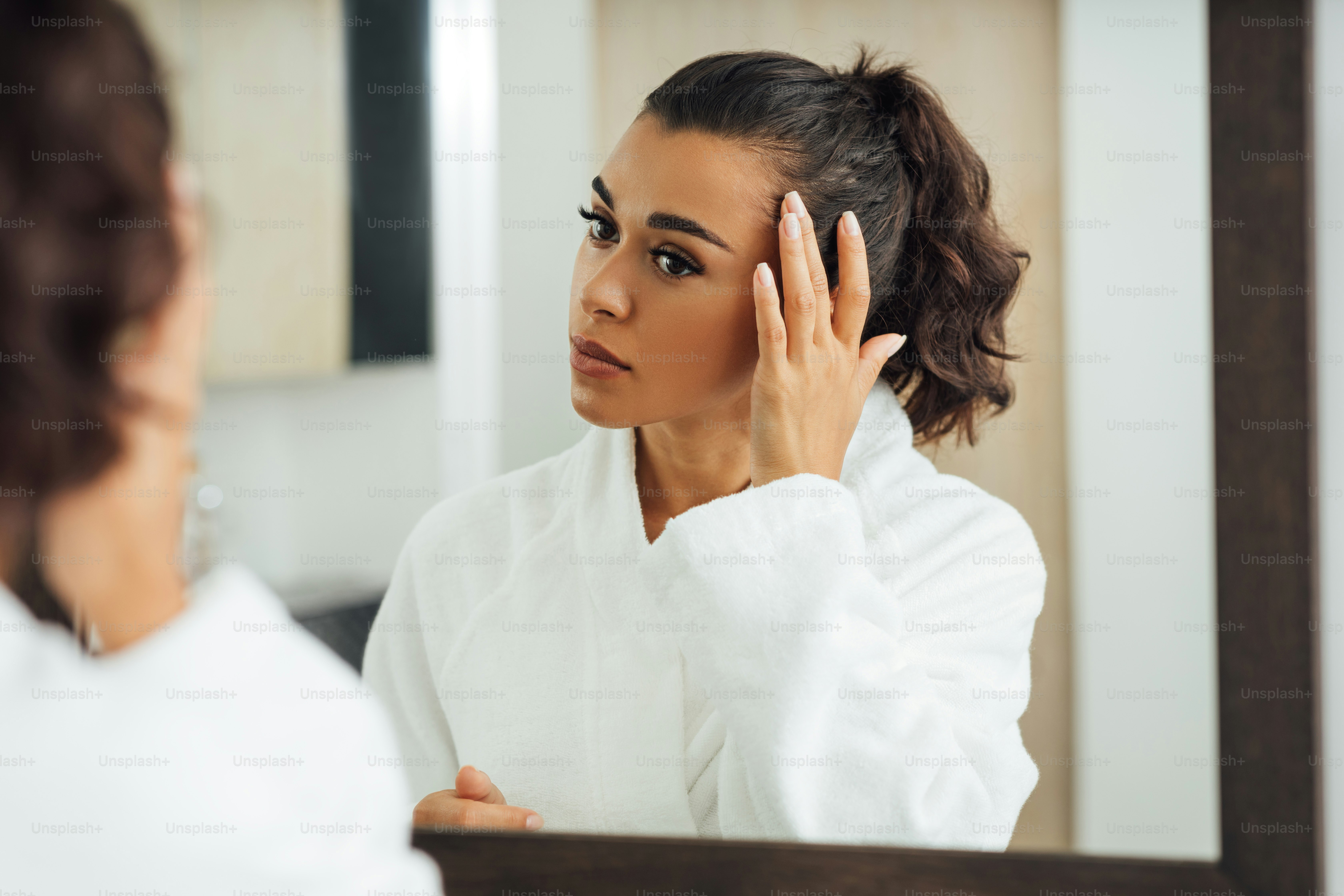 Beautiful brunette looking at reflection in the mirror and touching hair