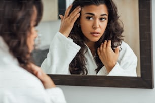 Middle East woman looking at mirror reflection taking care of her skin in bathroom