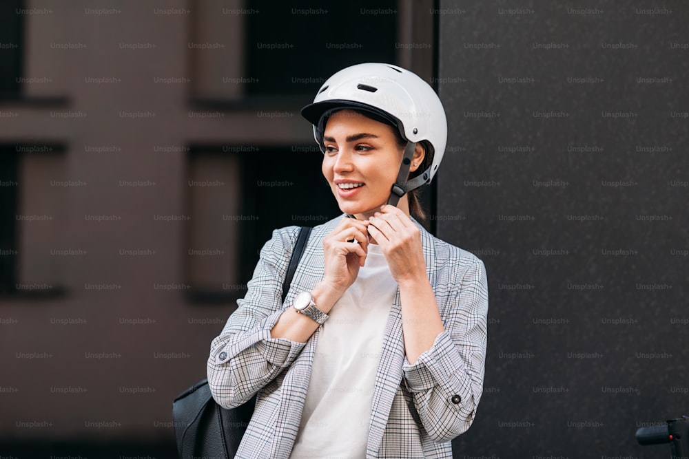 젊은 웃는 여자는 머리에 안전 헬멧을 착용합니다. 전기 스쿠터를 탈 준비를 하고 있는 사업가.