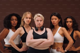 Cinco mujeres seguras de sí mismas en ropa deportiva de pie juntas. Mujeres de diferentes tipos de cuerpo mirando a la cámara.