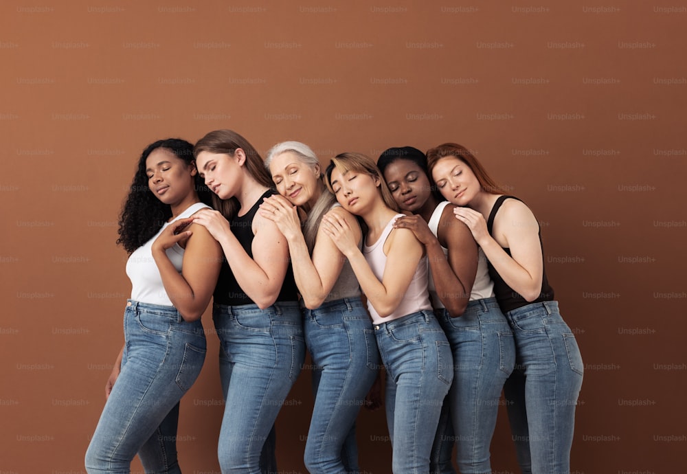 Diverse women in casuals embracing each other while standing with closed eyes over brown background