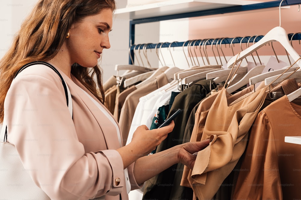 Side view of woman standing at a rack in clothing store scans the barcode using the mobile phone