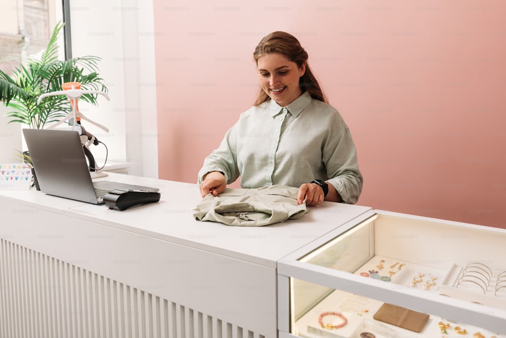 Saleswoman arranging clothes on a counter in store. Clothing store owner working at a table.