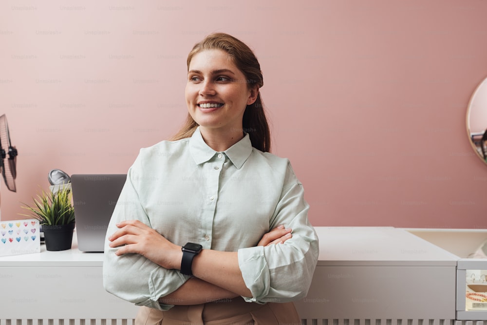 Smiling boutique owner standing at counter with crossed arms looking away