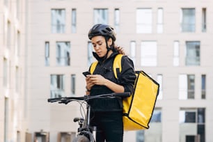 Woman courier with backpack checking information for delivery in the city