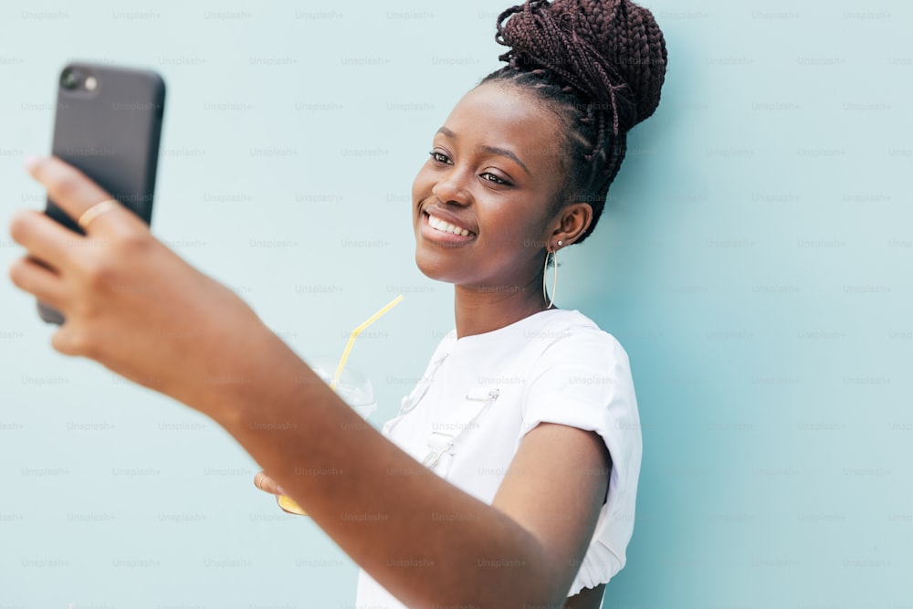 Happy woman in white clothes taking selfie near blue wall outdoors