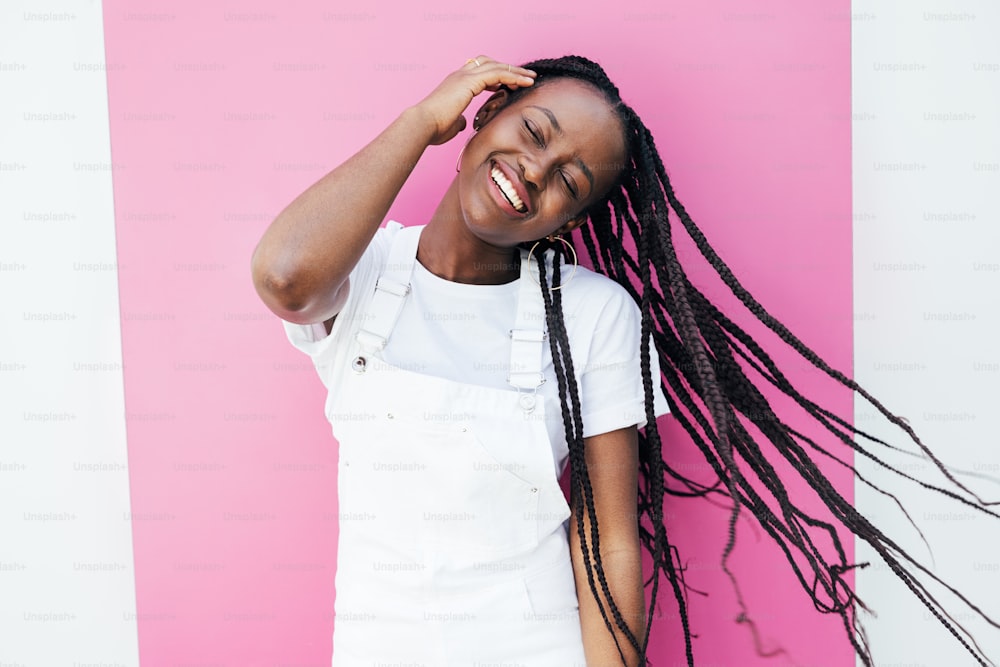 Retrato de una mujer sonriente positiva en casuales divirtiéndose mientras está parada en la pared rosa