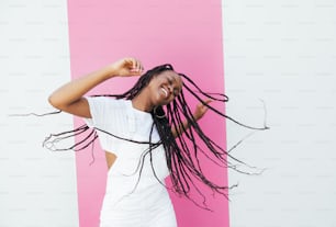 Donna giocosa con i capelli lunghi intrecciati che ballano su una parete bianca con striscia rosa