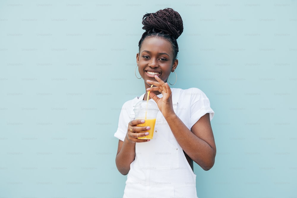 Young cheerful woman drinking a juice against blue wall and looking at camera
