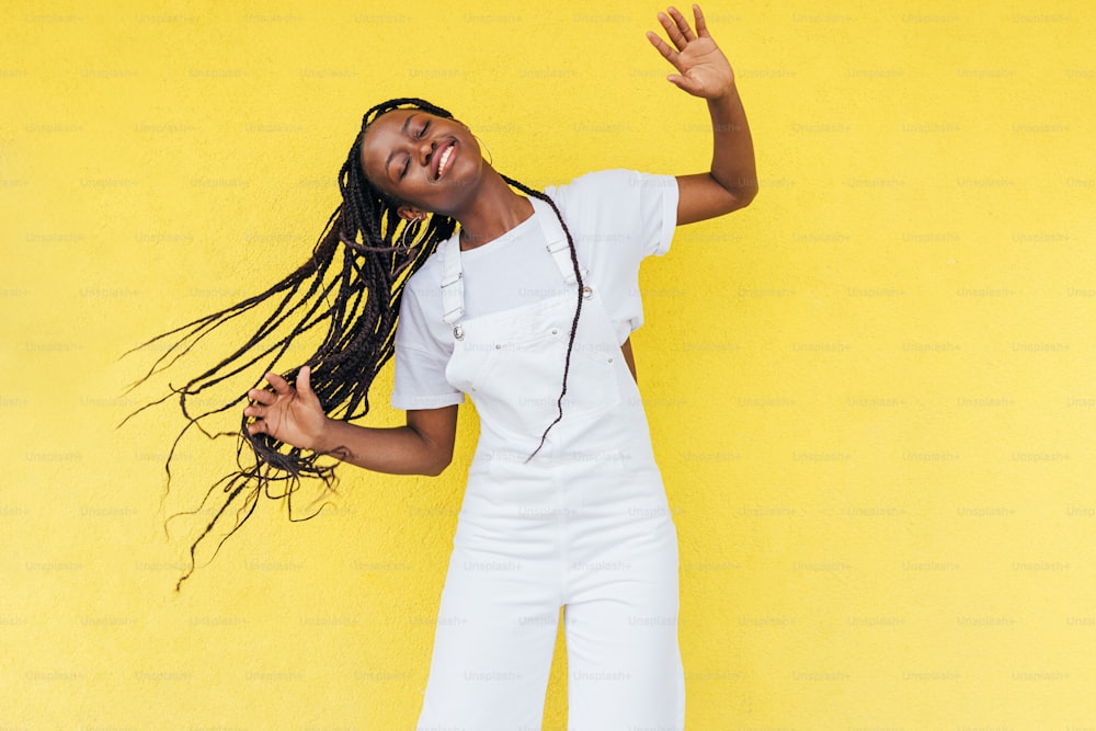 Cheerful woman wearing white overall dancing at yellow wall