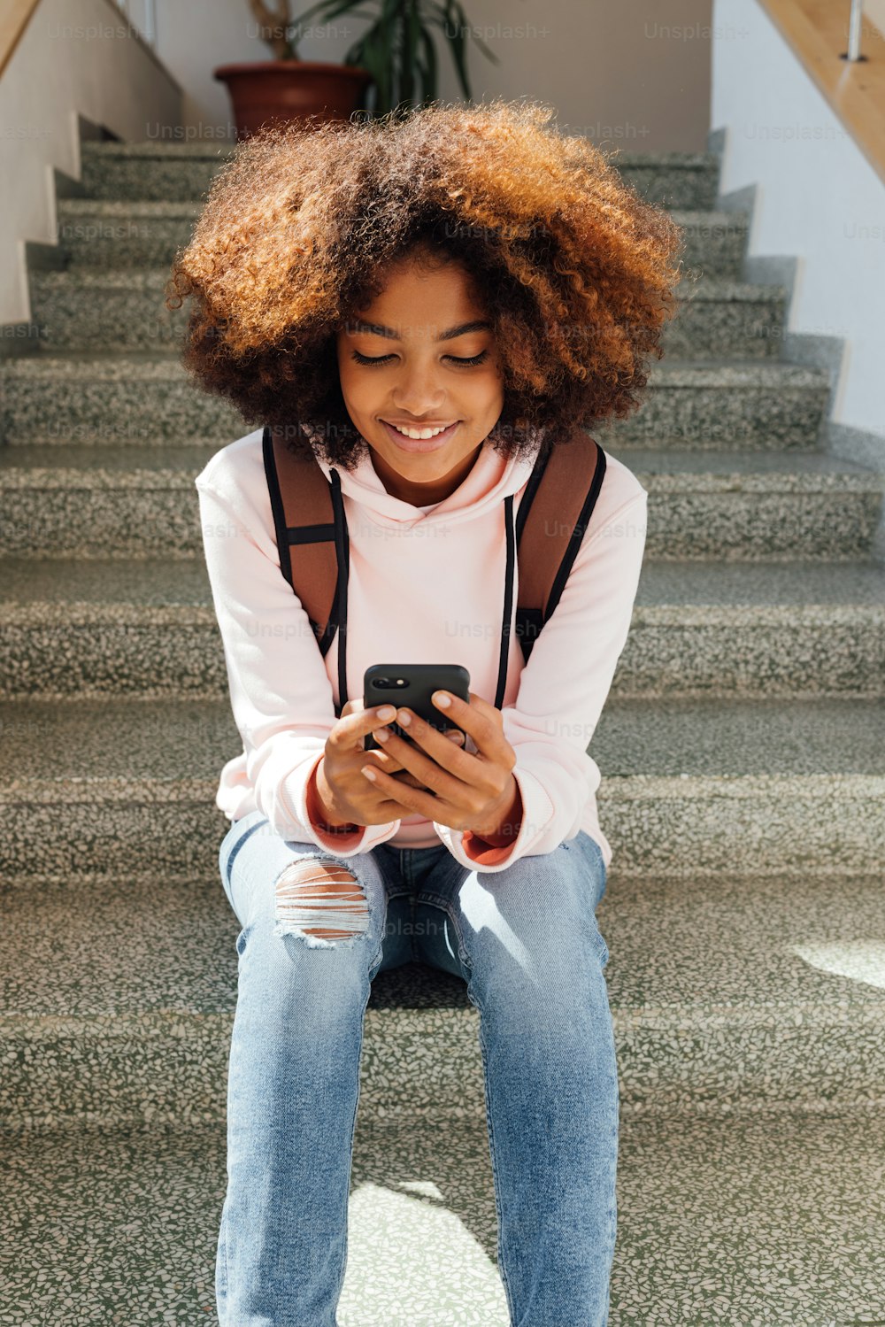 Smiling girl sitting on stairs in school and using smartphone