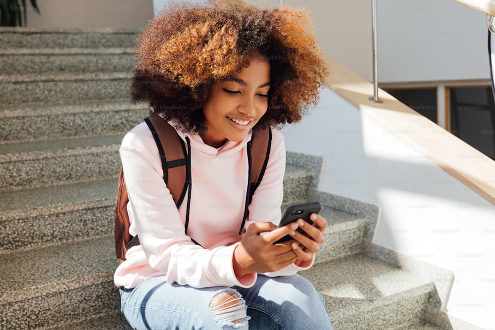 スマートフォンを持つ学校の階段に座っているカジュアルな笑顔の女の子のポートレート