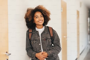Jovem estudante com mochila sorrindo no ensino médio encostando uma parede
