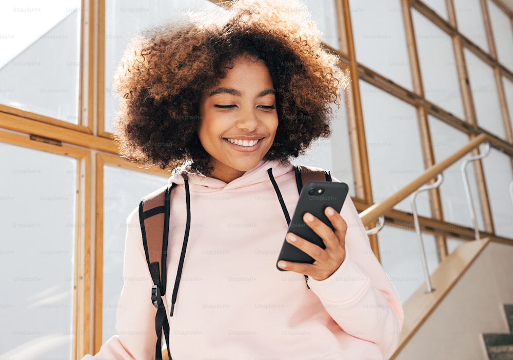 Cheerful girl in casuals looking at smartphone while standing in school
